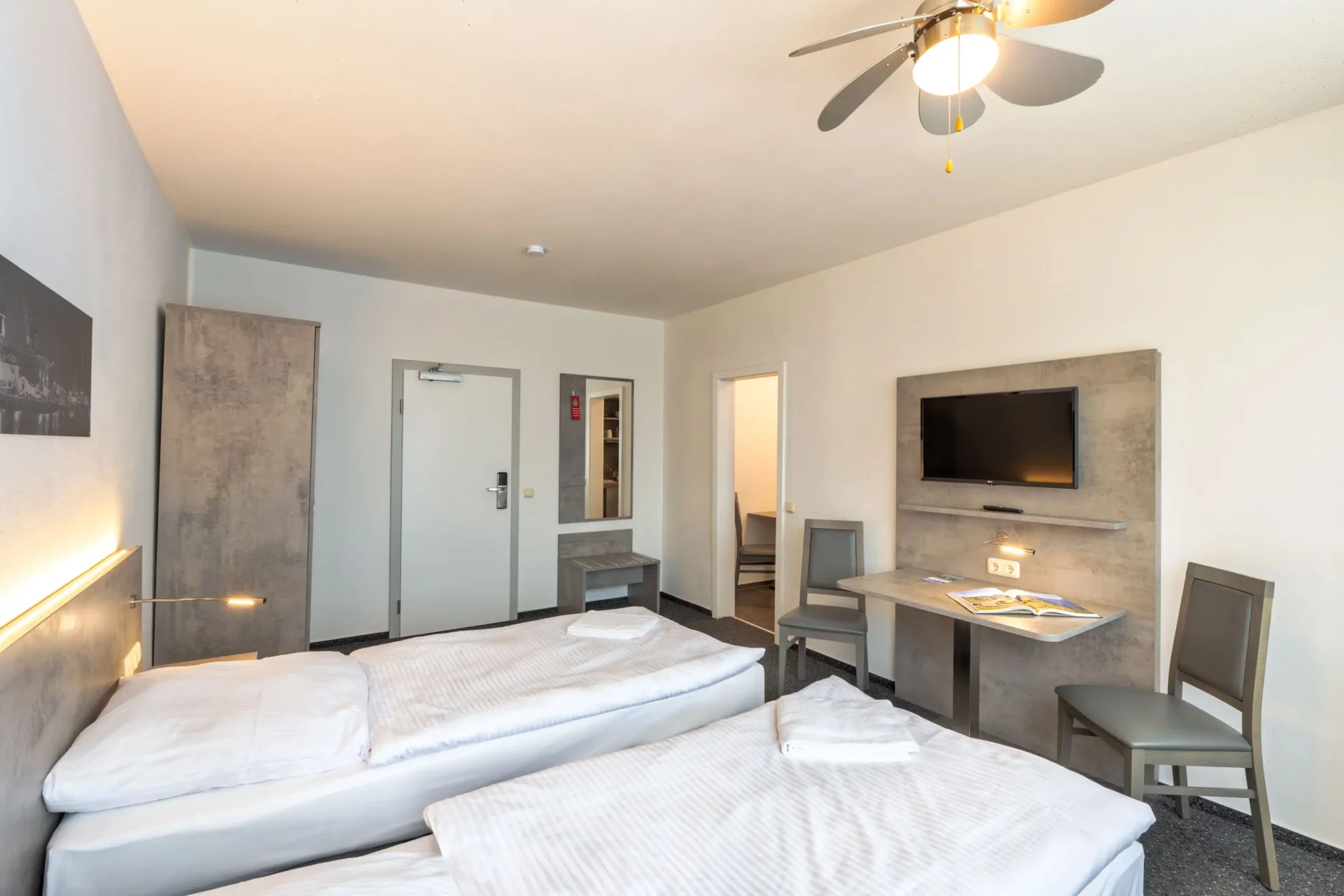 Großes, helles Zweibettzimmer mit Küche, Spiegel, Waschbecken, Tisch und Stühlen – Gemeinschaftsbad vorhanden.